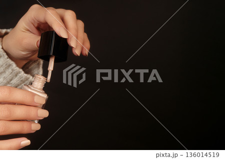 Female hands with pale nude nail design. Beige nails manicure. Woman hands hold latte color nail gel polish bottle on black background. Mockup style with copy space for Beauty salon. Manicured fingers 136014519