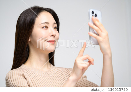 白背景でスマホを操作する女性 136015730