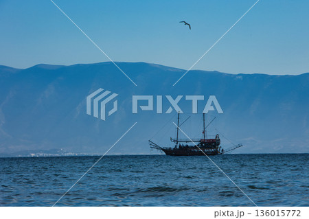Vlore, Albania August 24 2025 A tourist pirate-style boat sails across the calm blue sea with distant mountains forming a soft silhouette on the horizon. Vlore, Albania August 24 2025 A tourist pirate-style boat sails across the calm blue sea with distant mountains forming a soft silhouette on the horizon. 136015772