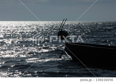 Silhouetted fishing boat on the shore of Vlora, Albania, captured on August 24, 2025. The backlit scene shows shimmering sunlight on the sea, gentle waves, and a swimmer in the background, creating a Silhouetted fishing boat on the shore of Vlora, Albania, captured on August 24, 2025. The backlit scene shows shimmering sunlight on the sea, gentle waves, and a swimmer in the background, creating a 136016056