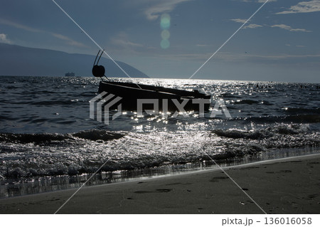 Silhouetted fishing boat on the shore of Vlora, Albania, captured on August 24, 2025. The backlit scene shows shimmering sunlight on the sea, gentle waves, and a swimmer in the background, creating a Silhouetted fishing boat on the shore of Vlora, Albania, captured on August 24, 2025. The backlit scene shows shimmering sunlight on the sea, gentle waves, and a swimmer in the background, creating a 136016058