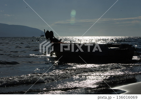 Silhouetted fishing boat on the shore of Vlora, Albania, captured on August 24, 2025. The backlit scene shows shimmering sunlight on the sea, gentle waves, and a swimmer in the background, creating a Silhouetted fishing boat on the shore of Vlora, Albania, captured on August 24, 2025. The backlit scene shows shimmering sunlight on the sea, gentle waves, and a swimmer in the background, creating a 136016069