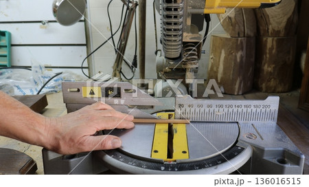 A carpenter's workstation and the working part of a miter saw during the process of measuring and sawing a small thin stick of joint, processing tiny wooden parts on a trimming machine A carpenter's workstation and the working part of a miter saw during the process of measuring and sawing a small thin stick of joint, processing tiny wooden parts on a trimming machine 136016515