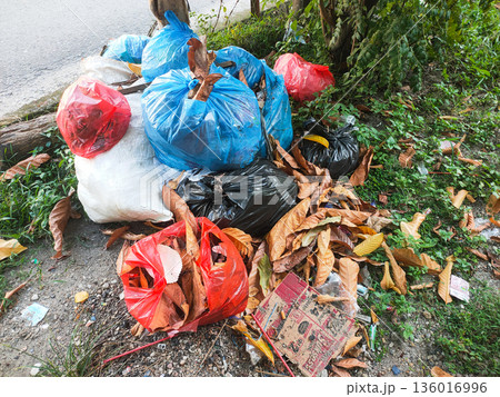Pile of colorful garbage bags dumped on roadside causing environmental pollution 136016996