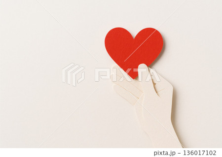 A paper hand holds a red heart, a symbol of love and care. Space for text. 136017102