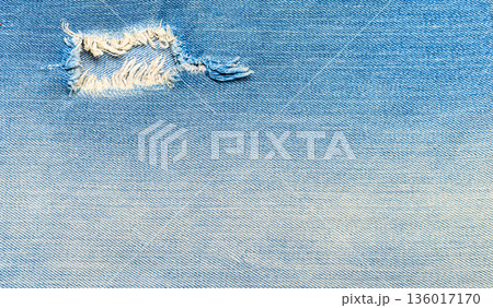 Distressed blue denim fabric texture with ripped hole Distressed blue denim fabric texture with ripped hole 136017170