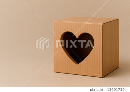 Cardboard box with a heart cut out on a beige background. Space for text. 136017394