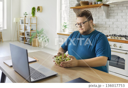 Plus-size man having diet salad at home kitchen during remote work time today 136017753
