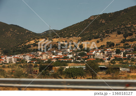 Hillside village landscape captured from the road in August 2025, showing traditional houses scattered across dry Mediterranean mountains under a calm summer sky. Hillside village landscape captured from the road in August 2025, showing traditional houses scattered across dry Mediterranean mountains under a calm summer sky. 136018127