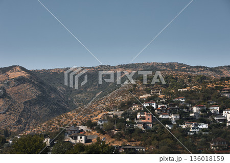 Hillside village landscape captured from the road in August 2025, showing traditional houses scattered across dry Mediterranean mountains under a calm summer sky. 136018159