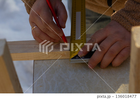 Craftsperson hands accurately measuring a wooden plank with a ruler and marking it with a red pencil, demonstrating precision in woodworking and construction. Craftsperson hands accurately measuring a wooden plank with a ruler and marking it with a red pencil, demonstrating precision in woodworking and construction. 136018477