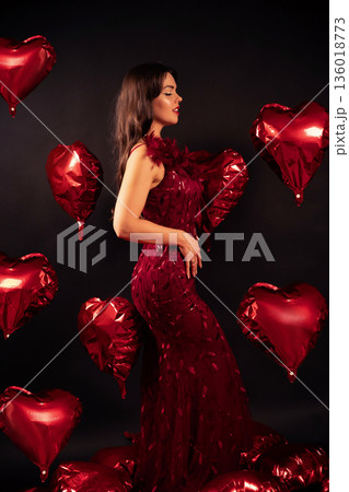 Woman in red dress surrounded by red heart balloons for Valentines Day celebration in studio setting Woman in red dress surrounded by red heart balloons for Valentines Day celebration in studio setting 136018773