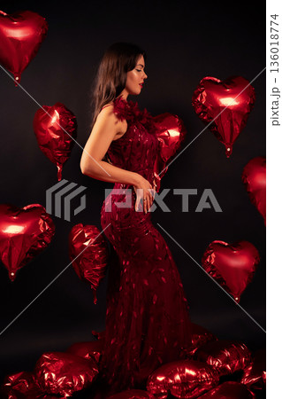 Beautiful woman in a red dress stands in front of heart balloons for Valentines Day celebration Beautiful woman in a red dress stands in front of heart balloons for Valentines Day celebration 136018774