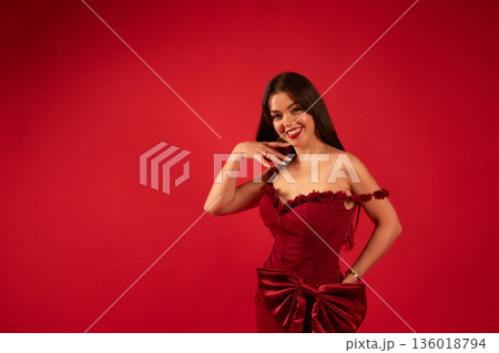 Beautiful woman smiles in red dress for celebration of love on Valentines Day in a bright red setting Beautiful woman smiles in red dress for celebration of love on Valentines Day in a bright red setting 136018794