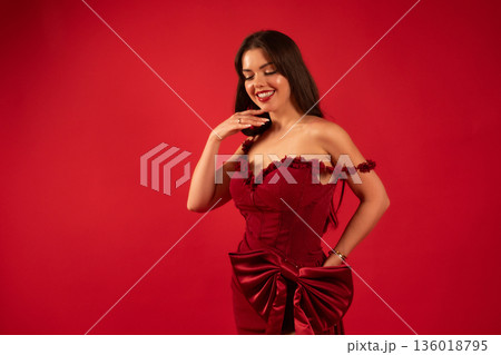 Woman in red dress smiles and poses for Valentines Day celebration in a studio setting with a simple background Woman in red dress smiles and poses for Valentines Day celebration in a studio setting with a simple background 136018795