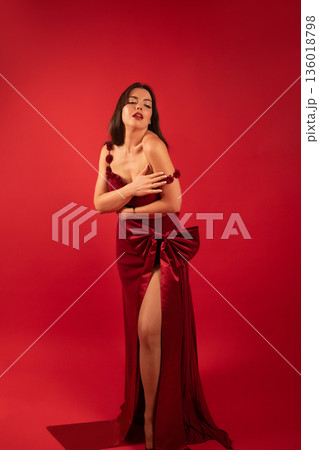 Woman in red dress poses against red background, expressing confidence and beauty for Valentines Day celebration 136018798