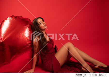 Woman in red dress poses next to heart decoration for Valentines Day celebration in indoor setting Woman in red dress poses next to heart decoration for Valentines Day celebration in indoor setting 136018826