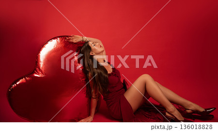 Woman poses in red dress next to heart-shaped balloon for Valentines Day celebration Woman poses in red dress next to heart-shaped balloon for Valentines Day celebration 136018828