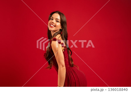 Woman in a red dress smiles on Valentines Day against a red background in a studio setting Woman in a red dress smiles on Valentines Day against a red background in a studio setting 136018840