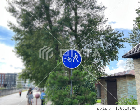 Round blue road sign with pedestrian and bicycle, blurred pedestrian road and cyclists in the background 136019309