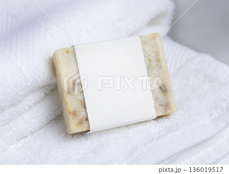 Cream soap bar with blank label on white bath towels near basin, natural hygiene product mockup 136019517
