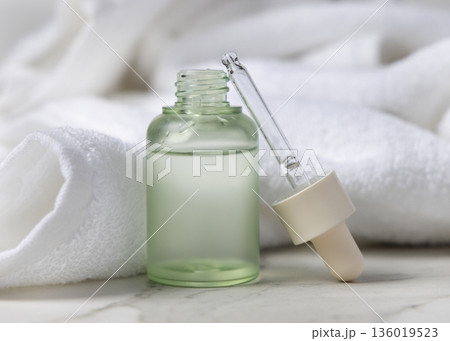 Pipette next to opened green glass dropper bottle near white bath towel, cosmetic mockup Pipette next to opened green glass dropper bottle near white bath towel, cosmetic mockup 136019523