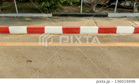 Red and white painted curb separating asphalt road from sidewalk Red and white painted curb separating asphalt road from sidewalk 136019896