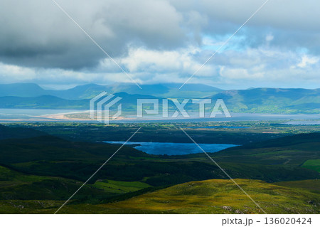 Green hills and forests meet a blue lake. Landscape with forests, water, and mountains. 136020424
