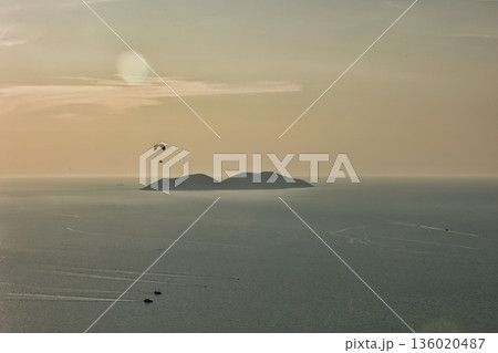 Mountain range rising above a calm blue sea under a clear sky, forming a minimalistic coastal landscape. Serene natural scenery captured on August  2025. 136020487