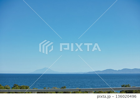 Mountain range rising above a calm blue sea under a clear sky, forming a minimalistic coastal landscape. Serene natural scenery captured on August 2025. Mountain range rising above a calm blue sea under a clear sky, forming a minimalistic coastal landscape. Serene natural scenery captured on August 2025. 136020496