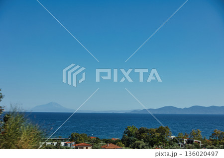 Mountain range rising above a calm blue sea under a clear sky, forming a minimalistic coastal landscape. Serene natural scenery captured on August 2025. Mountain range rising above a calm blue sea under a clear sky, forming a minimalistic coastal landscape. Serene natural scenery captured on August 2025. 136020497