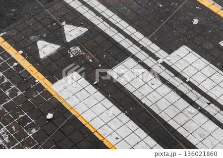 A close-up top view of a dark tiled sidewalk featuring bold white arrows and line 136021860