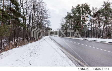 A quiet winter scene features a snow-dusted road winding through a forest A quiet winter scene features a snow-dusted road winding through a forest 136021863