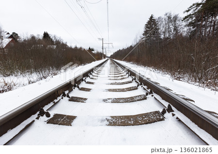 Snow-covered railway tracks extend toward the horizon, flanked by bare trees 136021865