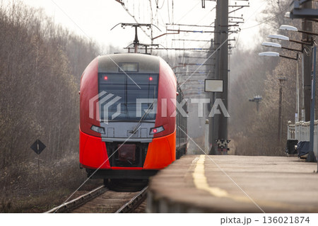 A sleek red modern train pulls into a quiet platform 136021874