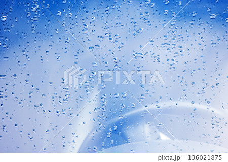 Close-up of droplets on a car glass reflecting a blue sky 136021875