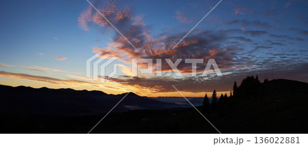 Breathtaking sunset paints sky with vibrant hues of pink, orange, purple, blending into blue morning sky. Silhouetted mountains, pine trees create serene backdrop. Tranquil and picturesque landscape. Breathtaking sunset paints sky with vibrant hues of pink, orange, purple, blending into blue morning sky. Silhouetted mountains, pine trees create serene backdrop. Tranquil and picturesque landscape. 136022881