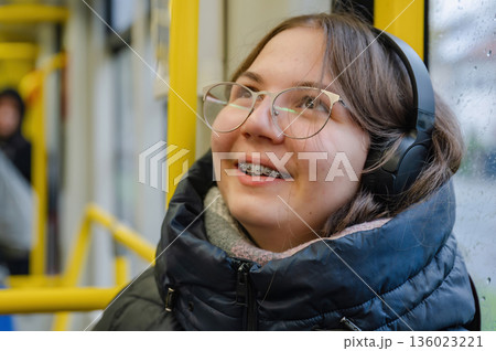 Smiling teenager girl with braces and headphones in tram during rainy weather Smiling teenager girl with braces and headphones in tram during rainy weather 136023221