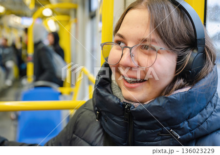 Smiling teenager girl with braces and headphones in tram during rainy weather 136023229