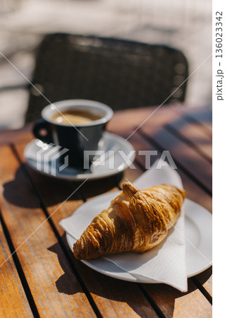 Cup of black coffee and a croissant on a table in a street cafe. Cup of black coffee and a croissant on a table in a street cafe. 136023342