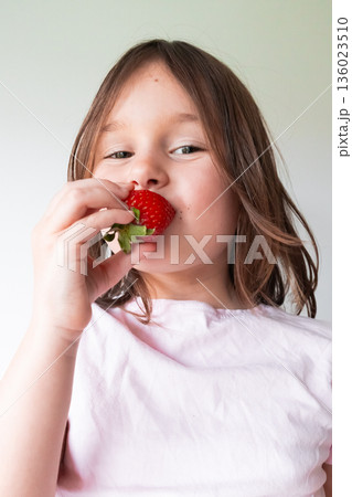 Caucasian young girl enjoying fresh strawberry in bright white setting Caucasian young girl enjoying fresh strawberry in bright white setting 136023510