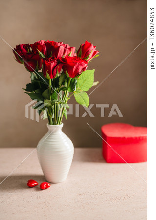 Valentine's Day festive background. Red roses flowers in a vase and heart gift box on the table. Festive greeting card, flat lay 136024853