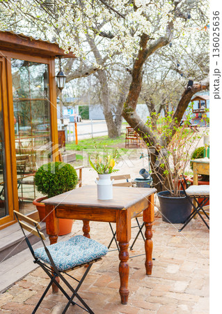 Spring outdoor garden table with bouquet of flowers under blooming trees in cozy backyard cafe 136025636