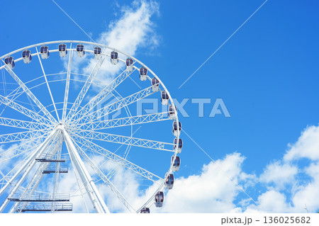 Large ferris wheel against blue sky with white clouds on sunny day Large ferris wheel against blue sky with white clouds on sunny day 136025682