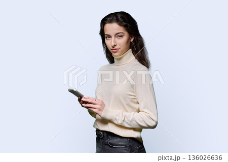 Portrait of serious teenage girl holding smartphone on white studio background Portrait of serious teenage girl holding smartphone on white studio background 136026636