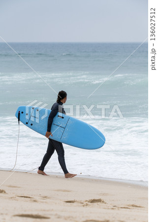 Surfer girl carrying a soft board Surfer girl carrying a soft board 136027512