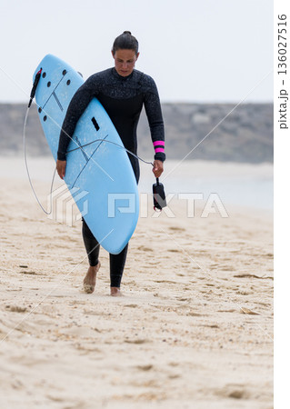 Surfer girl carrying a soft board Surfer girl carrying a soft board 136027516