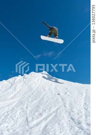 Snowboarder jumping against blue sky Snowboarder jumping against blue sky 136027795