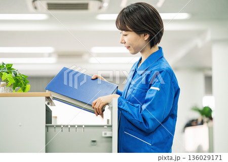 オフィスでファイルを片付ける作業服姿の若い女性 136029171