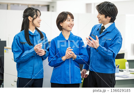 オフィスで話をする青い作業服を着た若い男女 オフィスで話をする青い作業服を着た若い男女 136029185